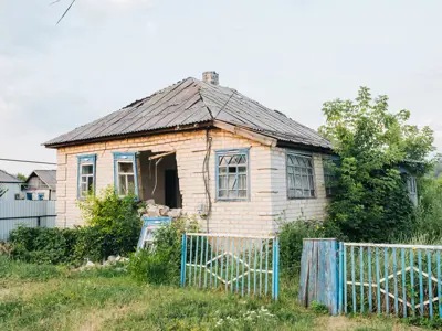 Abandoned structurally damaged building and fence with weeds in yard