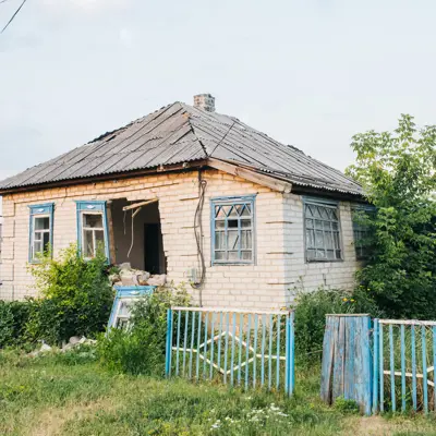Abandoned structurally damaged building and fence with weeds in yard
