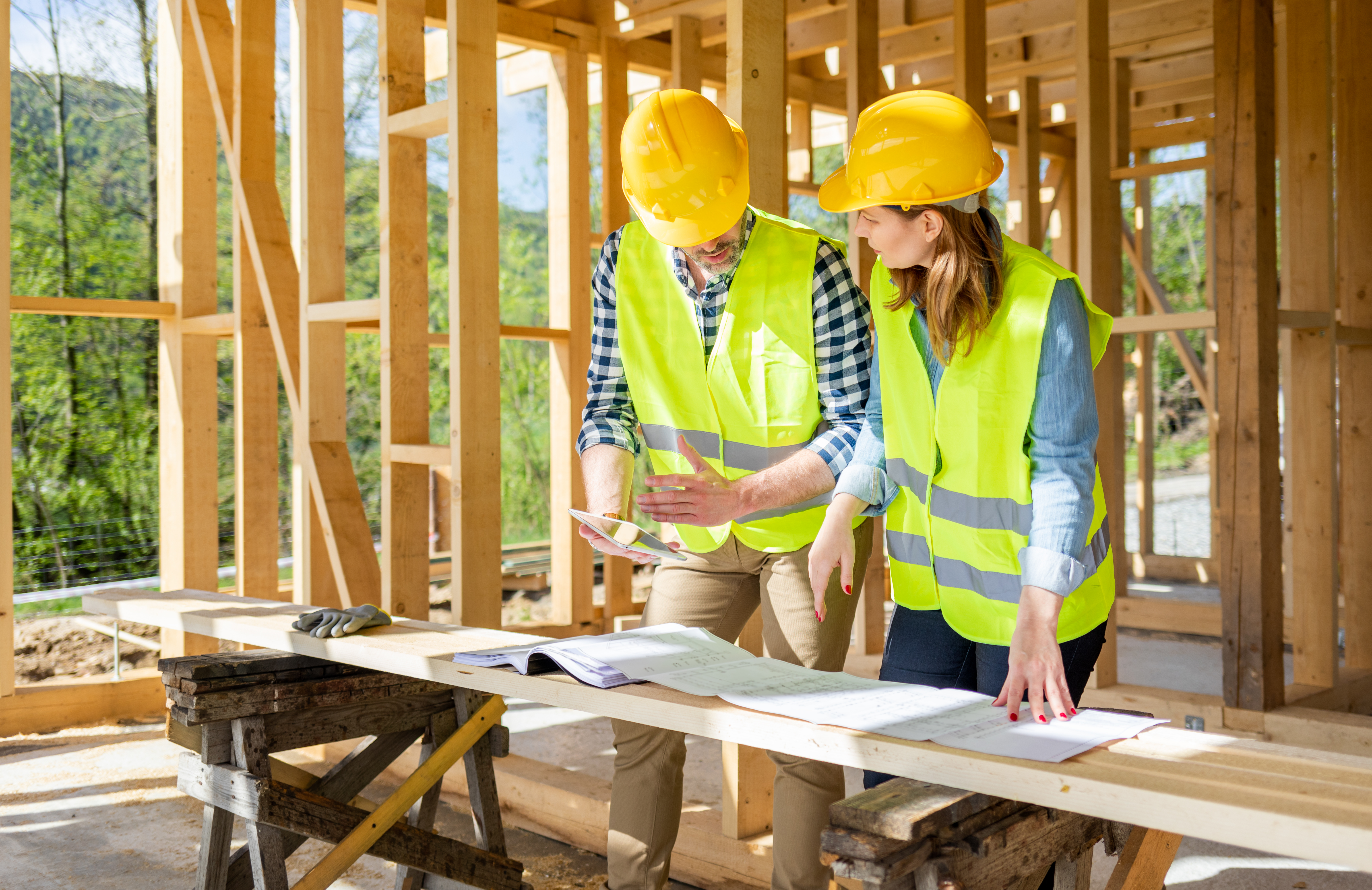 Man and woman construction workers looking at building plans in a wood framed building under construction