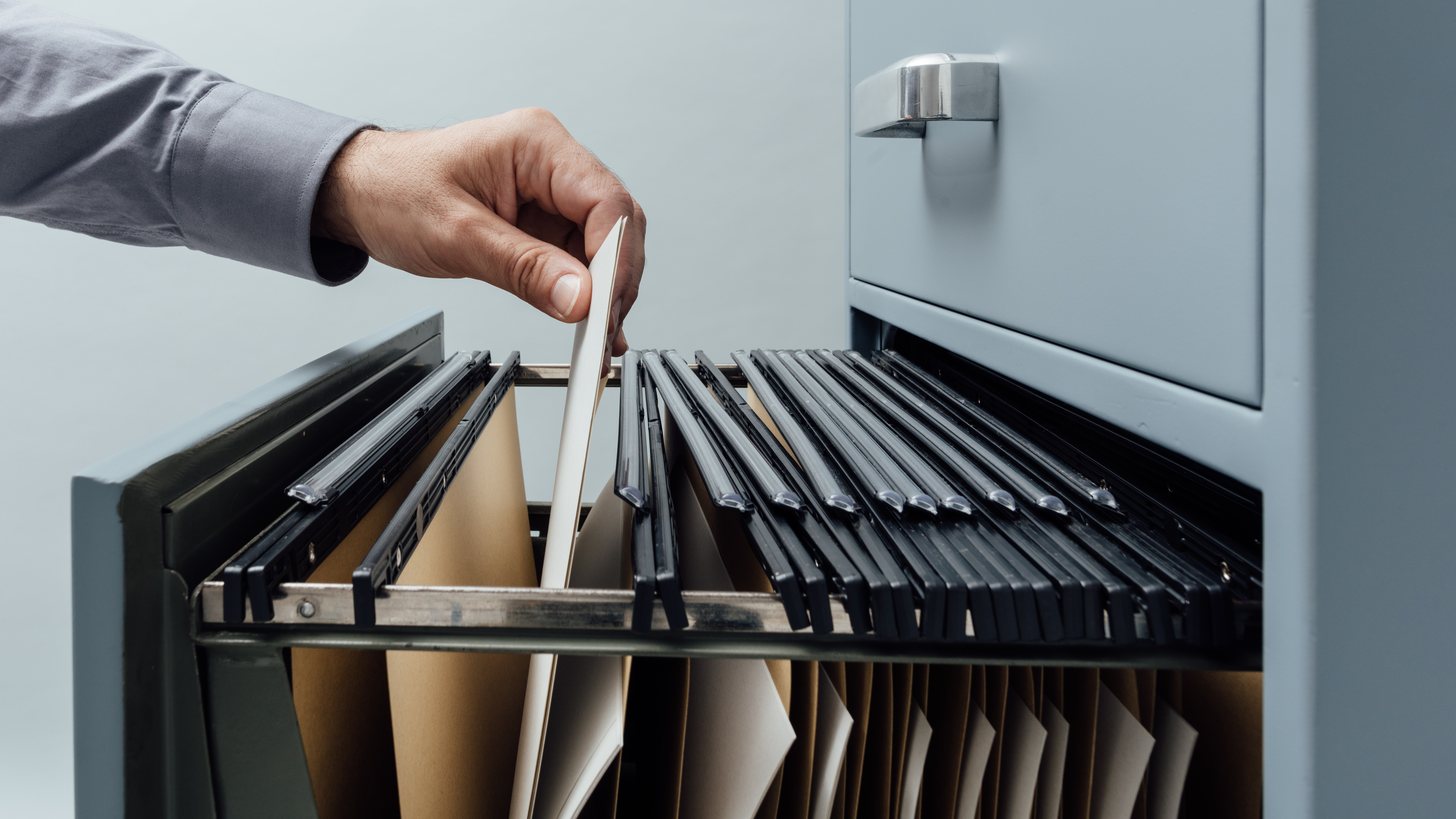 A hand removing a file from an open filing cabinet drawer. 
