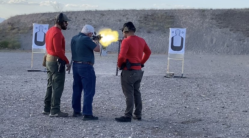man shooting a rifle at the range with police officers