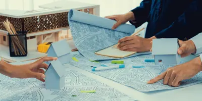 Arms and hands of three people standing at a table holding paperwork with house models