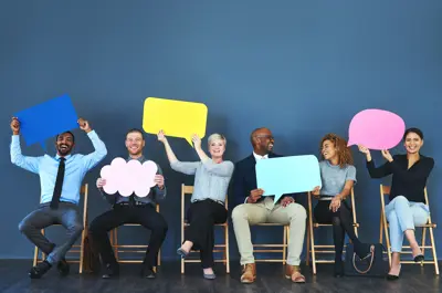 Line of people sitting in chairs each holding a giant piece of paper cut in the shape of a dialog box from a comic.